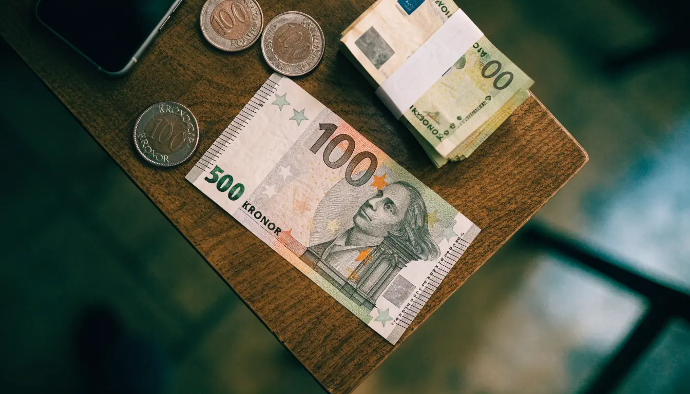 Femtio euro sedel bredvid svenska kronor mynt och sedlar på ett träbord